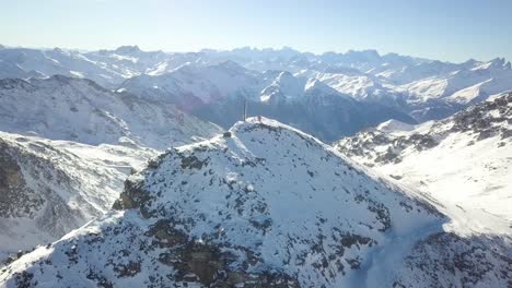 Snow-capped-Majestic-Mountain-Peak-in-Val-Thorens-with-two-skiers-on-top,-French-Alps---Aerial-Orbit-descending-360-shot