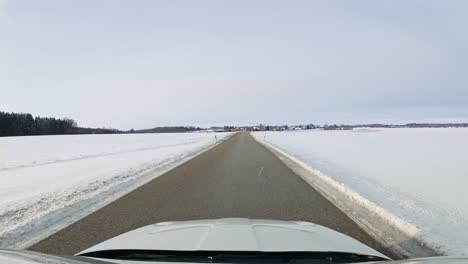 Driving-through-a-snowy-landscape-along-a-straight-road-by-car-in-windshield-view-at-a-cold-winter-day
