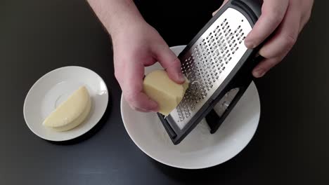 Hände-Reiben-Käse-Mit-Einer-Reibe-In-Einen-Teller