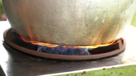 Stainless-steel-pot-on-burning-flame-boiling-water,-close-up-handheld-view