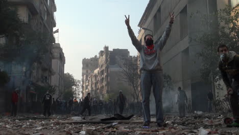 Protestors-man-a-barricade,-standing-in-defiance-giving-peace-hand-signals-and-throw-a-tear-gas-canister-back-at-security-forces-on-a-street-in-Cairo-during-clashes-in-the-Egyptian-revolution
