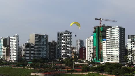 4k-aerial-video-of-paragliders-flying-incredibly-close-to-the-coastline-of-Miraflores-in-Lima,-Peru