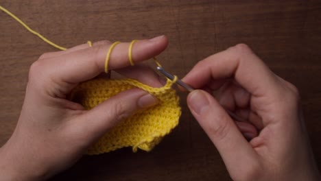 Top-shot-of-a-female-holding-a-piece-of-yellow-wool-and-a-needle
