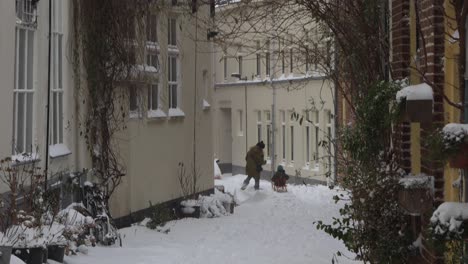 Snowing-scene-in-The-Netherlands-with-a-young-family-of-which-the-children-ride-a-sledge-that-their-parents-tow-in-a-small-alley-of-historic-city-centre