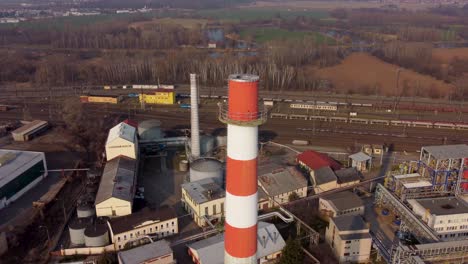 aerial-view-of-an-industrial-chimney-with-a-train-in-the-background,-flyover