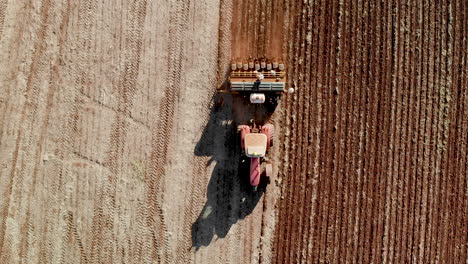 Aerial-view-shot-of-a-farmer-in-tractor-seeding,-sowing-agricultural-crops-at-field