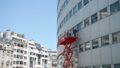 Arbeiter-Auf-Einer-Erhöhten-Plattform,-Die-Am-Fenster-An-Der-Außenseite-Des-Maison-De-La-Radio-Gebäudes-In-Paris,-Frankreich,-Arbeitet