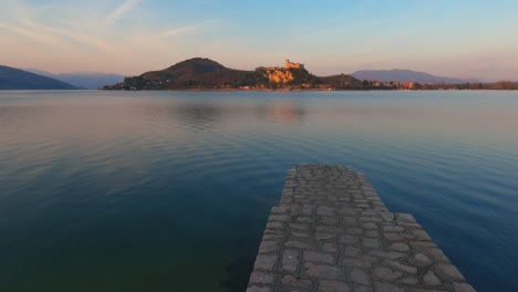 Peaceful-scene-of-concrete-dock-on-lake-Maggiore-calm-water-in-Italy,-Angera-castle-on-background