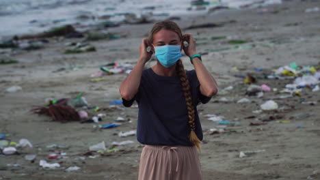 Woman-Smile-At-Camera-Then-Wear-A-Face-Mask-While-On-The-Beach-With-Trash