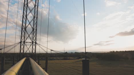 Walking-On-Narrow-Suspension-Bridge-Over-Field-On-A-Sunset