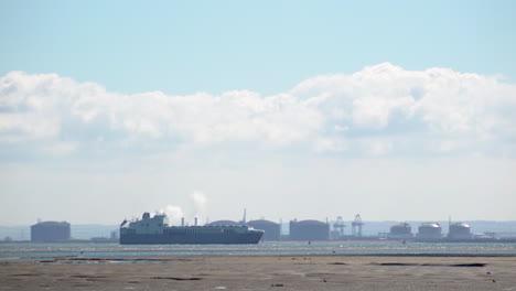 Time-lapse-of-a-cargo-ship-passing-an-oil-and-gas-refinery-on-the-Thames-estuary-near-Leigh-on-Sea-on-a-hot-and-sunny-early-spring-day