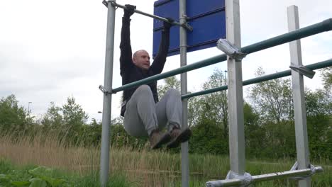 Man-Doing-Leg-Pull-Ups-On-Horizontal-Bar-And-Flexing-Abdominal-Muscles-Outdoors---wide-shot