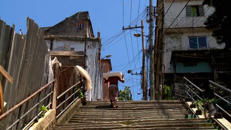 Mientras-Los-Cables-Eléctricos-Piratas-Cruzan-El-Cielo-Sobre-La-Favela,-Un-Hombre-Lleva-Una-Carga-Pesada-Por-Las-Escaleras