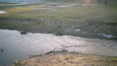 Pan-of-water-flowing-into-sewage-system-under-road-by-grass-field
