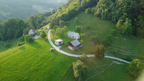 Flying-around-an-idyllic-small-farm-on-top-of-the-hill-surrounded-with-green-meadows-and-forest