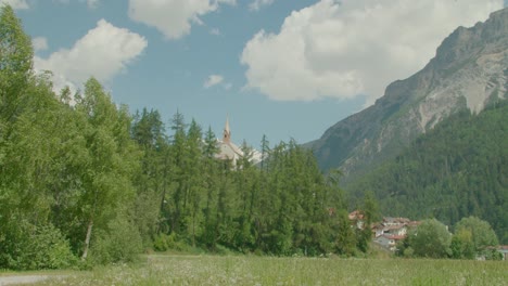 Totalaufnahme,-Malerische-Aussicht-Auf-Grasland-Und-Hohe-Bäume-In-Italien,-Kirchturm-Und-Bergkette-Neben-Dem-Reschensee-In-Südtirol