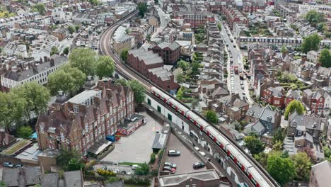Cinematic-drone-follow-shot-of-district-line-train-winding-through-residential-London-Putney-bridge