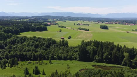 Idyllic-bavarian-summer-landscape,-filmed-from-above,-panning-right,-in-mountain-range-of-the-alps-with-a-little-pond-and-green-meadows-in-the-foreground