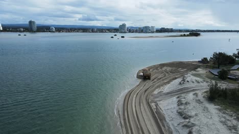 High-moving-drone-view-following-a-large-dump-truck-carrying-sand-along-a-coastal-beach-road