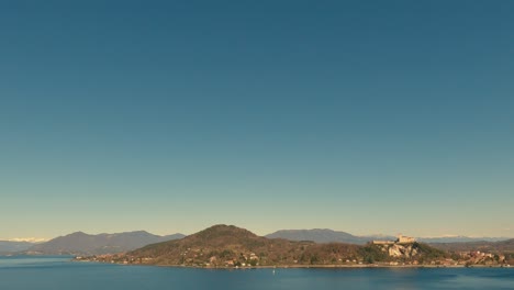 Panoramablick-Auf-Den-Wunderschönen-Lago-Maggiore-Und-Die-Festung-Von-Angera-Mit-Klarem-Himmel-Und-Boot,-Das-über-Ruhiges-Wasser-Segelt