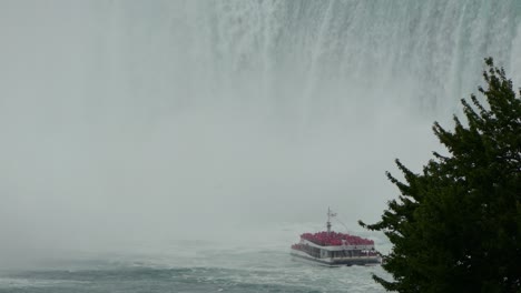 Niagara-Falls-tour-boat-near-waterfall-cascade-spray-mist,-popular-tourism
