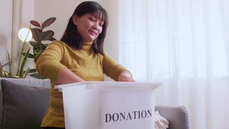 Asian-woman-selecting-clothes-for-donation-and-putting-them-in-a-box