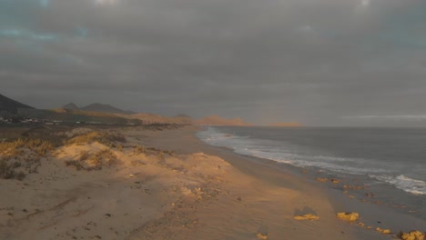 Aerial-forward-along-Calheta-beach-at-sunset-on-cloudy-day,-Portugal