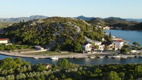 An-aerial-footage-in-summer-evening-following-river-fork-and-opening-on-village-houses-with-docked-boats-in-Rogotin,-south-Croatia-coast
