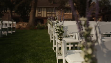 Dolly-back,-rack-focus,-beautiful-flowers-at-exterior-wedding-with-white-chairs
