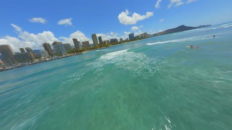 Flying-Towards-Diamond-Head-Hawaii,-FPV-Drone-Over-Surfers-in-Waikiki-With-Honolulu-Skyline-In-the-Background