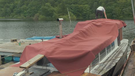 Junger-Mann-Sichert-Wasserdichte-Plane-über-Holzboot