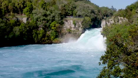 Tiny-people-in-the-distance-on-a-viewing-platform-enjoying-watching-the-giant-Huka-Falls-waterfall-on-a-day-out-in-Taupo,-New-Zealand-Aotearoa