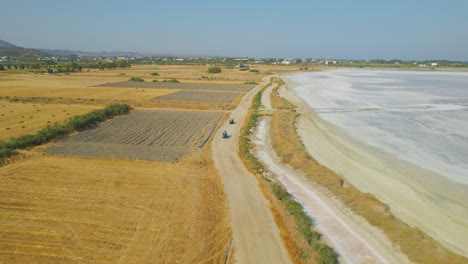 ATVs-driving-beside-salt-lake-in-Greek-countryside,-aerial-view