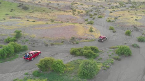 Aerial-Tracking-Shot-Of-Two-Red-Trucks-Riding-Across-Gravel-Path-In-Balochistan,-Pakistan