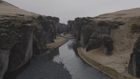 Aerial-forward-between-rock-walls-of-Fjadrargljufur-Canyon,-Iceland
