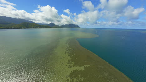 Flying-Over-Kaneohe-Bay-Oahu-Hawaii,-with-Mountains-and-Clouds-In-Background,-Gorgeous-Reef-and-Water-Below