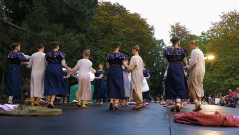 Adult-caucasian-female-dancers-in-traditional-folk-costumes-perform-in-a-dance-performance-in-open-air,-sunny-summer-evening,-happy,-Latvian-national-culture,-wide-handheld-low-angle-shot