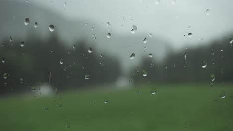 Rain-drops-on-window-glass-with-blurry-nature-background,-static-close-up-shot