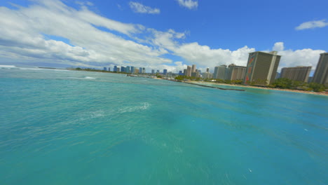 Flying-Over-Waves-on-Waikiki,-FPV-Drone-Flying-Over-Blue-Pacific-Water-Towards-Waikiki-and-Honolulu-on-Bright-Summer-Day