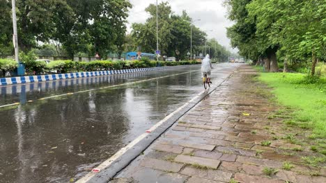 A-man-wearing-rain-coat-cycling-in-the-roads-of-Kolkata,-West-Bengal-after-heavy-rains-in-Kolkata-due-to-Yaas-cyclone