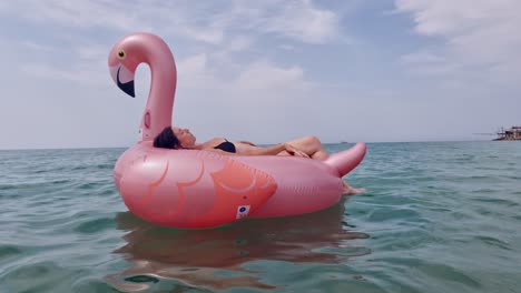 Woman-with-bikini-swimwear-relaxing-on-inflatable-pink-flamingo-floating-on-sea-water-surface