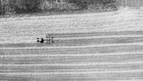 Tractor-with-its-twin-rotor-rake-trailer-working-on-a-farm-straight-from-above-in-black-and-white