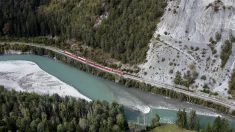 Red-train-drives-in-the-scenic-rhine-canyon-in-Switzerland,-aerial-view
