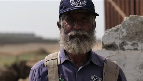 Älterer-Pakistanischer-Arbeiter-Mit-Weißem-Bart,-Baseballmütze-Und-Blick-In-Die-Kamera