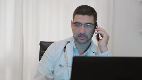 Male-Doctor-Talking-On-The-Phone-Inside-His-Clinic