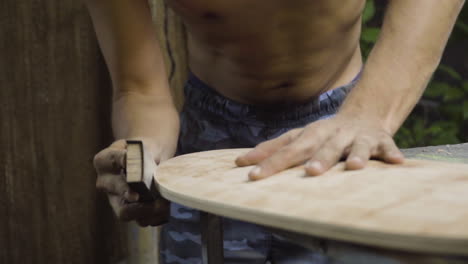 Worker-rubbing-sandpaper-for-smoothing-the-edges-and-giving-wood-finishing-to-new-skateboard