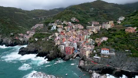 Italienischer-Nebliger-Morgen-In-Riomaggiore,-Cinque-Terre,-Italien-Mit-Bunten-Häusern-Und-Hafen-Entlang-Der-Felsigen-Küste-Mit-Tosenden-Wellen