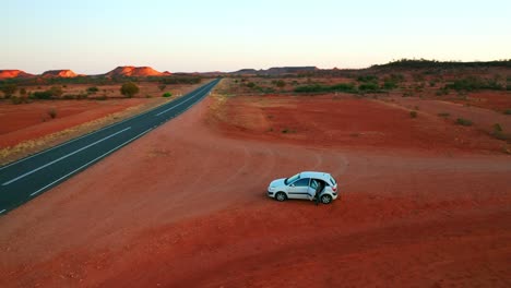 Orbiting-Aerial-View-of-a-car-on-a-roadside-of-Stuart-Highway-during-sunrise---NT,-Australia