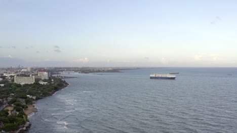 Drone-flying-over-sea-and-cargo-ship-in-background-near-Malecon,-Santo-Domingo