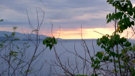 Ein-Blick-Auf-Ein-Boot-In-Der-Ferne,-Das-Bei-Einem-Atemberaubenden-Rosa,-Orangefarbenen,-Wolkigen-Sonnenuntergang-Auf-Einer-Abgelegenen-Tropischen-Insel-Ankert